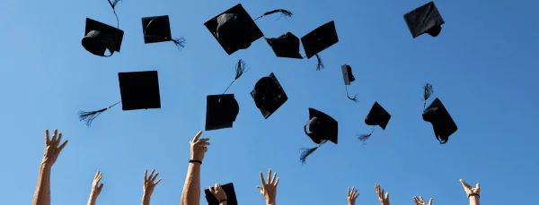 Graduates' hands throwing caps into the air against a clear blue sky, celebrating graduation.