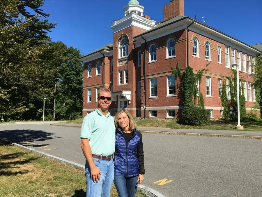 Kevin and Vicky stand together in front of a red brick building with a green dome, smiling on a sunny day.