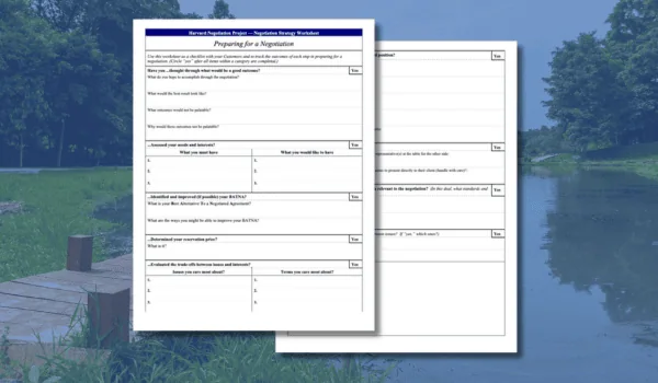 Two printed worksheets titled 'Preparing for a Negotiation' with questions and spaces for answers, placed on a wooden surface outdoors with a lake and trees in the background.