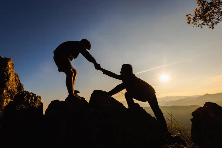 Silhouettes of two people climbing on mountain and helping. Help and assistance concept.