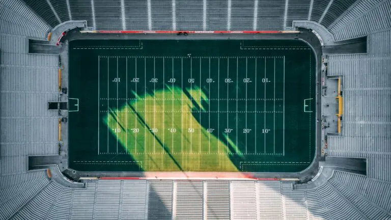 View of a football field from above, showing yard lines and a large green and yellow logo or design in the center.