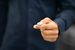 Close-up of a person in a dark shirt holding a small round white device between their thumb and index finger.