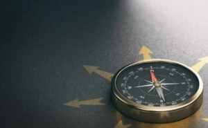 A compass on a dark surface with multiple arrows pointing in different directions, symbolizing guidance and direction.