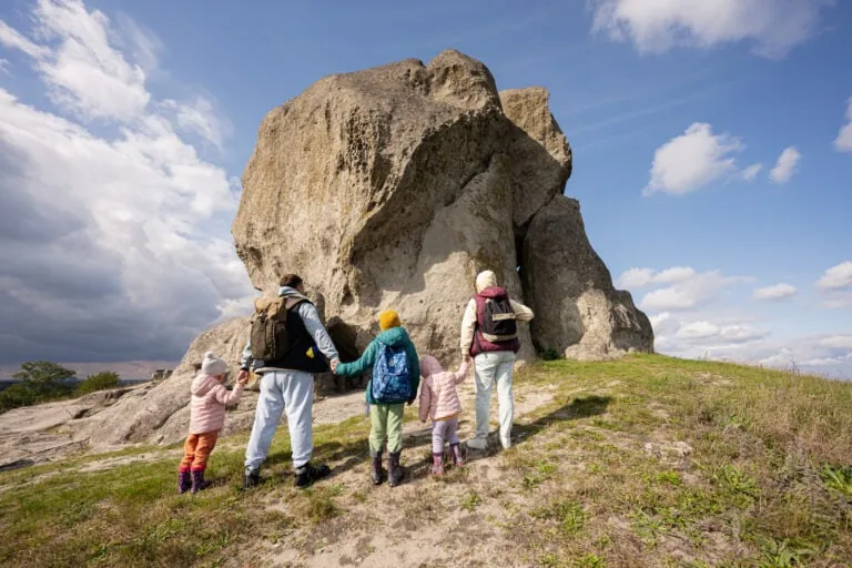 Family exploring nature. Children with parents wear backpack hiking against big stone in hill. Pidkamin, Ukraine.